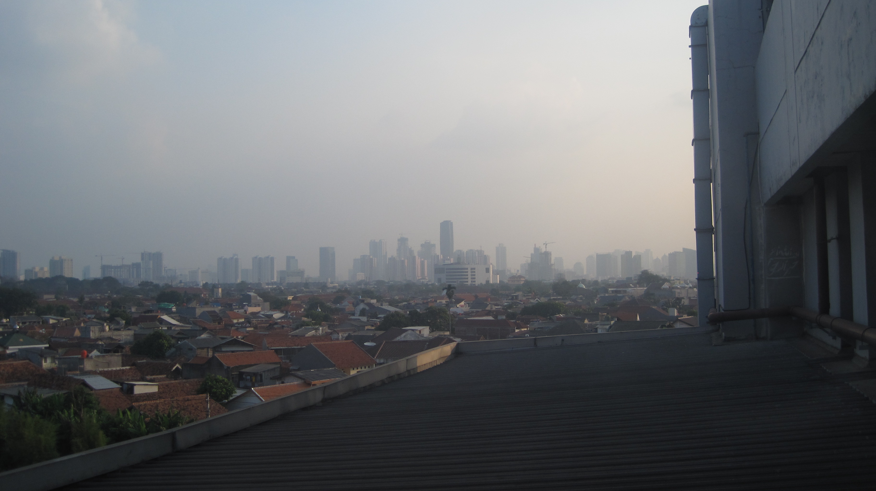 Hazy daytime skyline of Jakarta, Indonesia, with dense low-rise neighbourhoods and distant high-rises