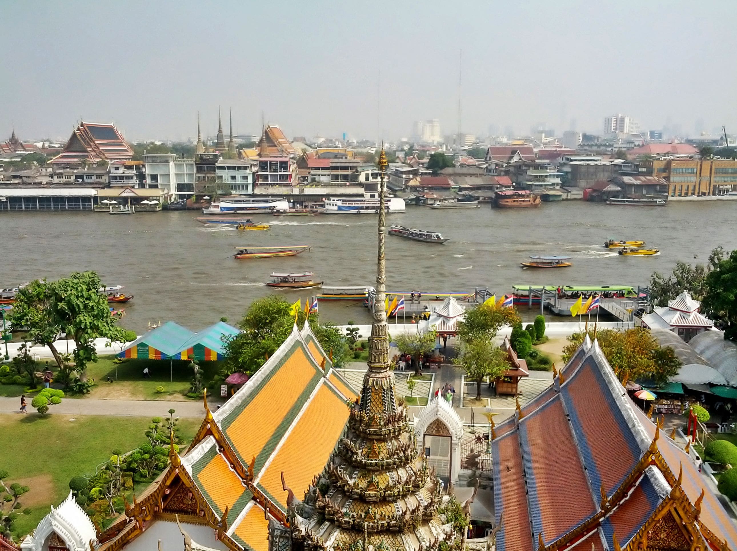View across the Chao Phraya River in Bangkok, Thailand, with temple roofs and boats on the water