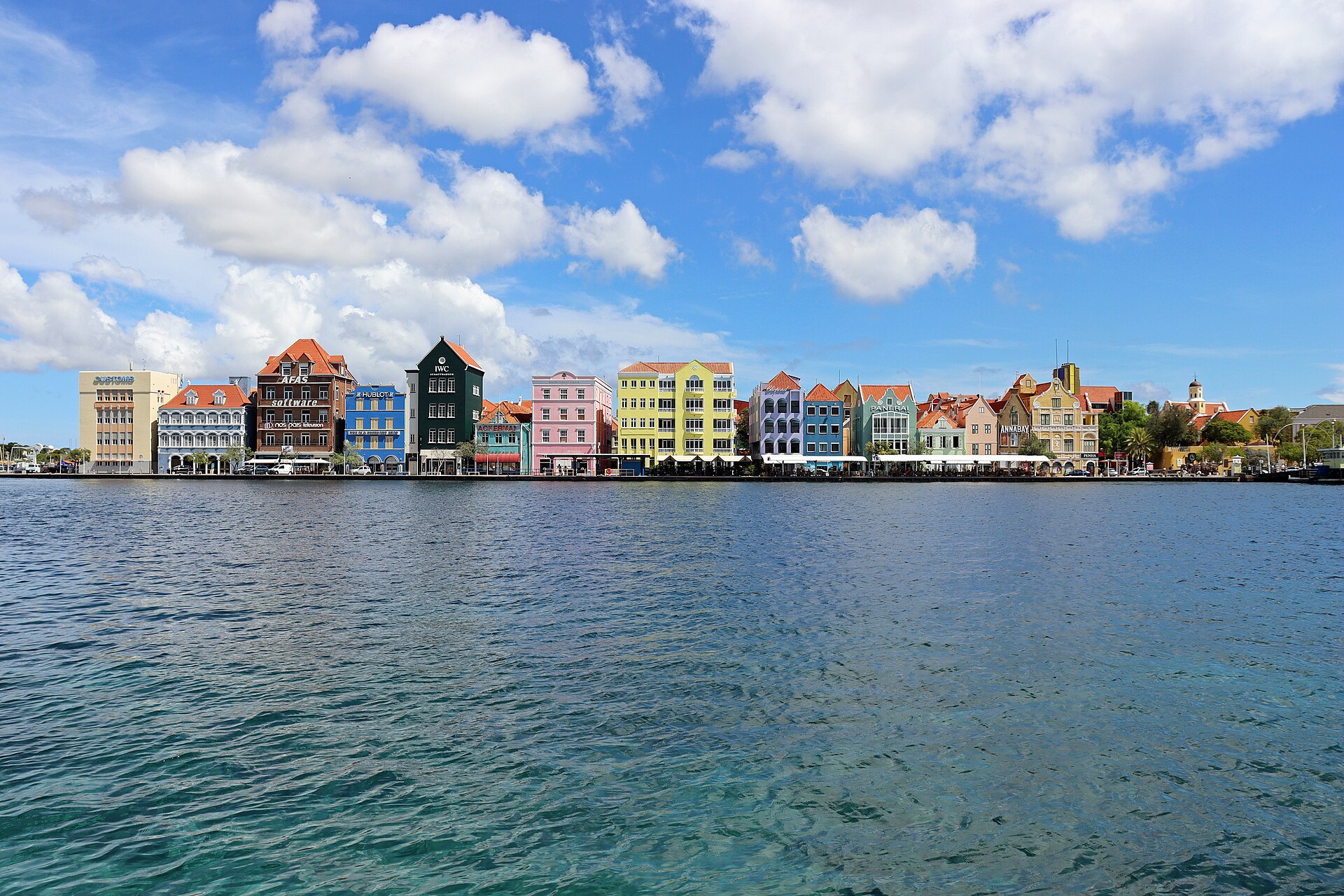 Colourful Dutch colonial-style waterfront buildings along the Handelskade in Willemstad, Curaçao, seen across the harbour under a blue sky