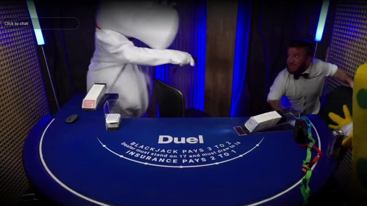 A person in a white costume and a male dealer struggle beside a Duel blackjack table as another costumed character looks on