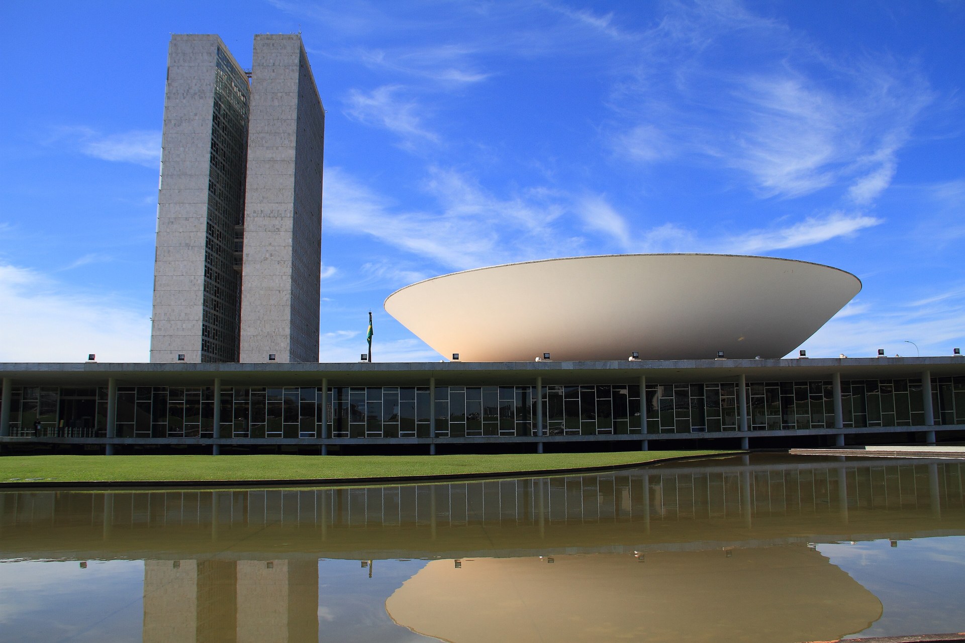 The twin towers and white domed chamber of Brazil's National Congress in Brasília, reflected in a pool under a blue sky