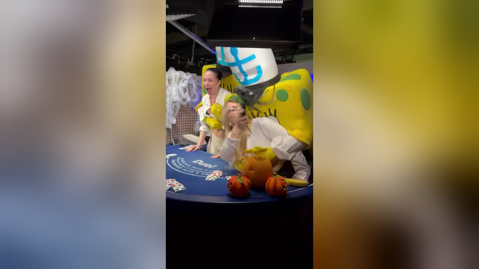 Two people in SpongeBob costumes lean over a live blackjack table decorated with Halloween pumpkins as two dealers react