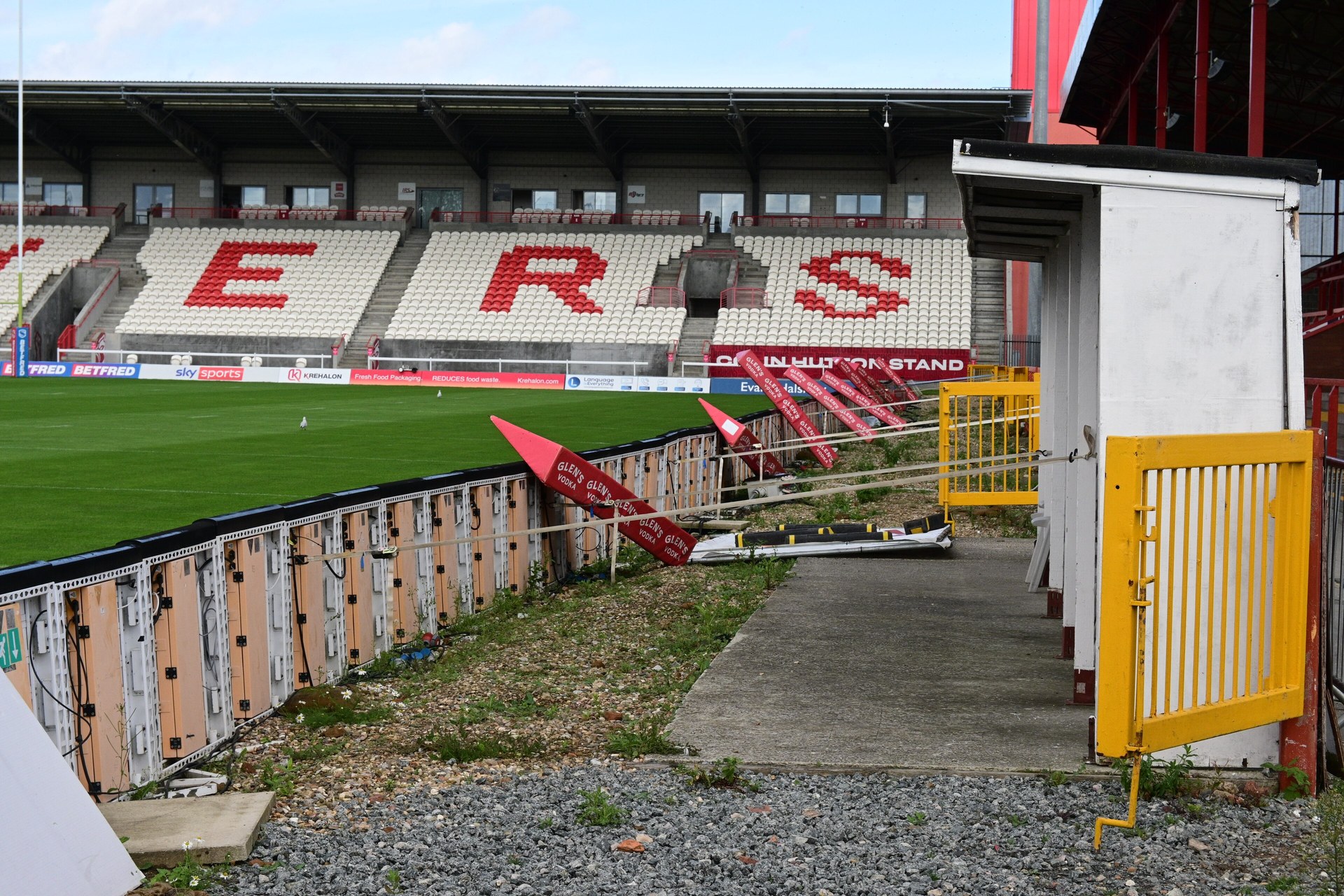 The backs of electronic advertising boards lining the pitch at a rugby league stadium, with empty stands behind