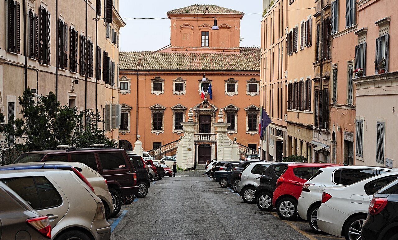 Via dell'Olmata in Rome, a street of terracotta-coloured buildings with parked cars and Italian and EU flags