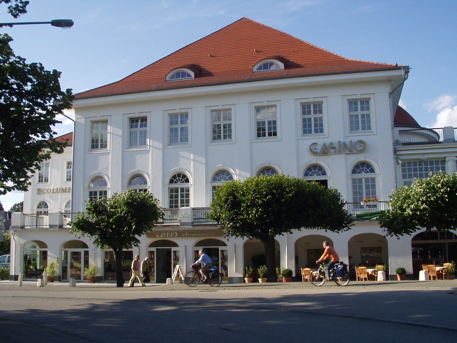 The white casino building on the seafront promenade at Travemünde, Lübeck, with cyclists passing in front
