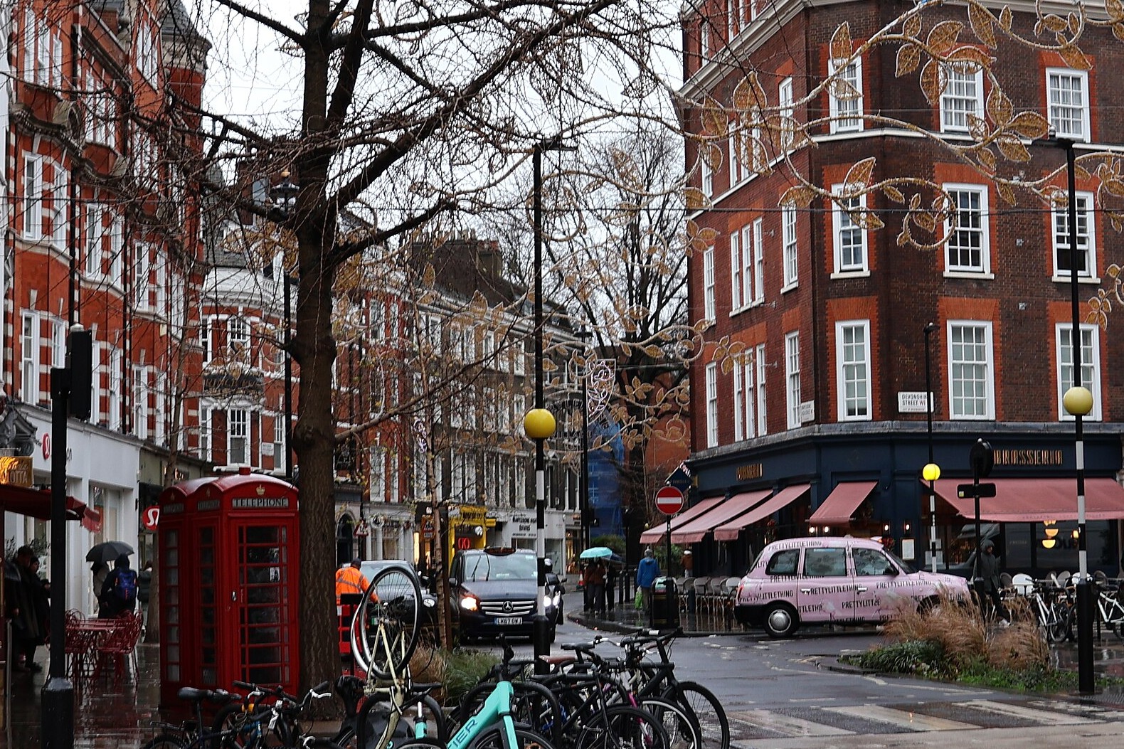 A wet British high street in Marylebone, London, with a red telephone box, parked bicycles and red-brick buildings